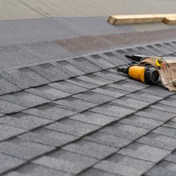Photo of toolbelt with instrument and nail gun lying on asphalt or bitumen shingle on top of the new roof under construction residential house or building